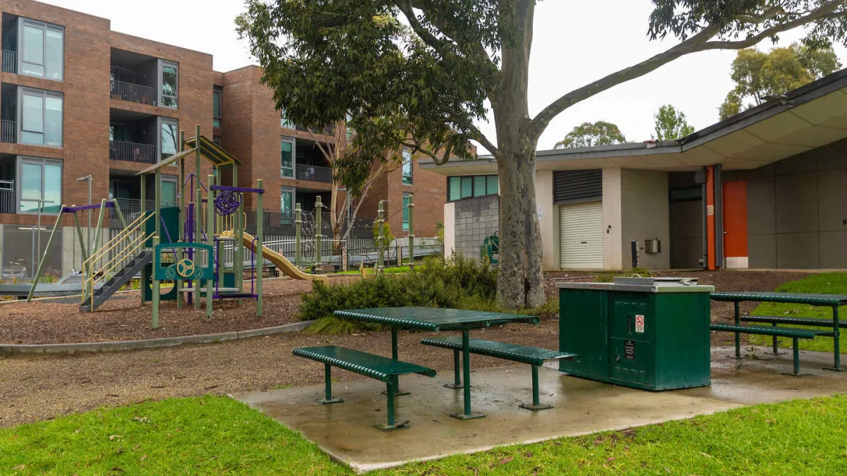 Park with a playground in the background and picnic tables and barbecue in the foreground