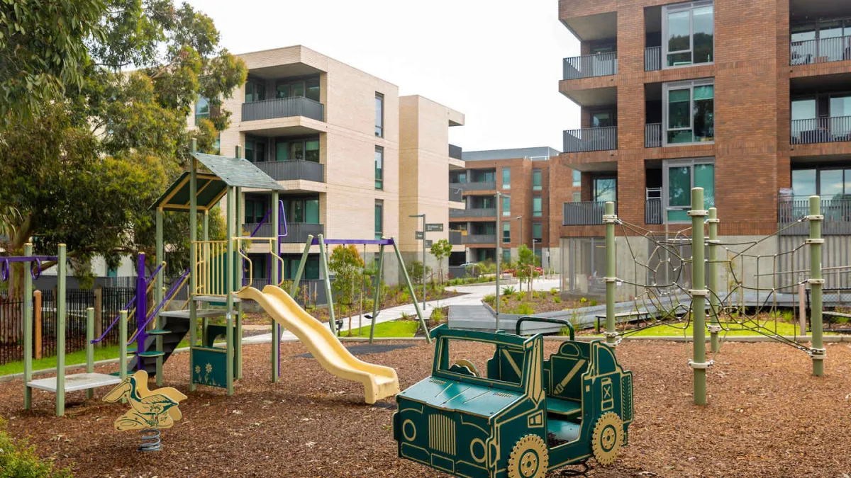 Playground featuring a slide and a vehicle. Apartment buildings in the background. 