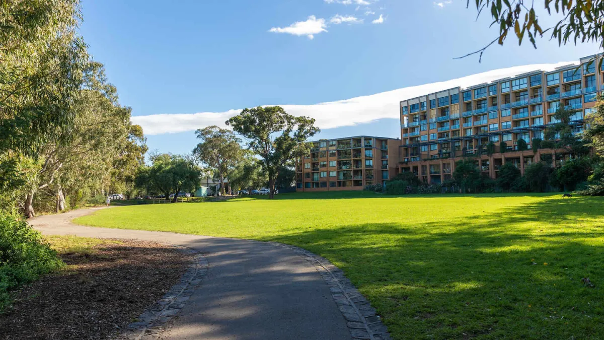 An open space park area. Trees and a walking path are on the left, a tall apartment building is to the right. 