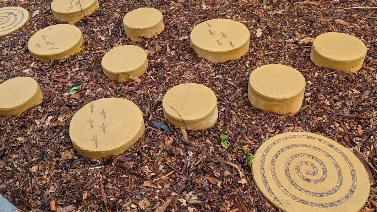 Concrete stepping pads rise out of tan bark at a playground