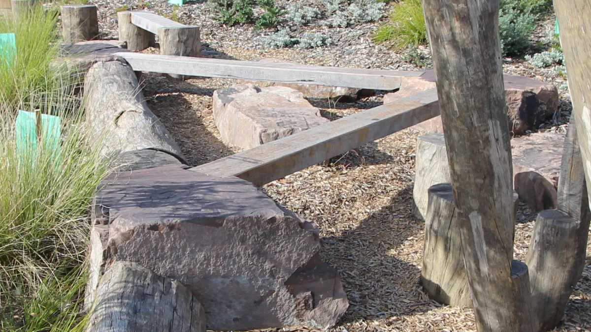 Timber beams balance on rocks as part of a nature play zone at a playground