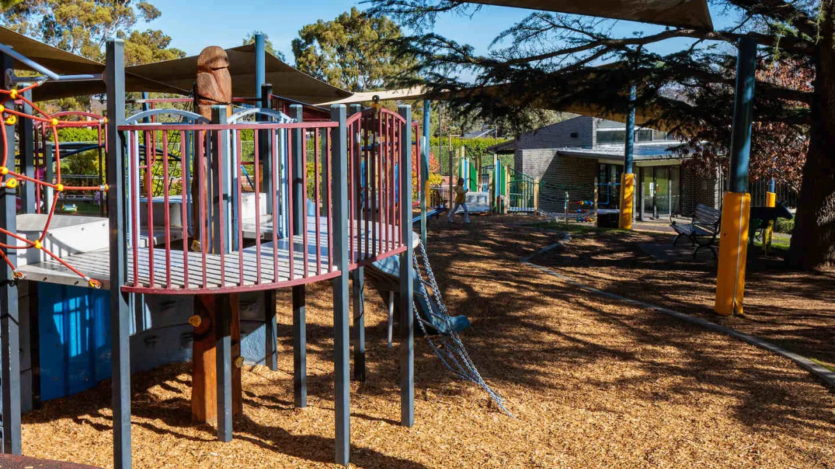 A children's playgound on a mulch surface. It is covered with shade sails. 
