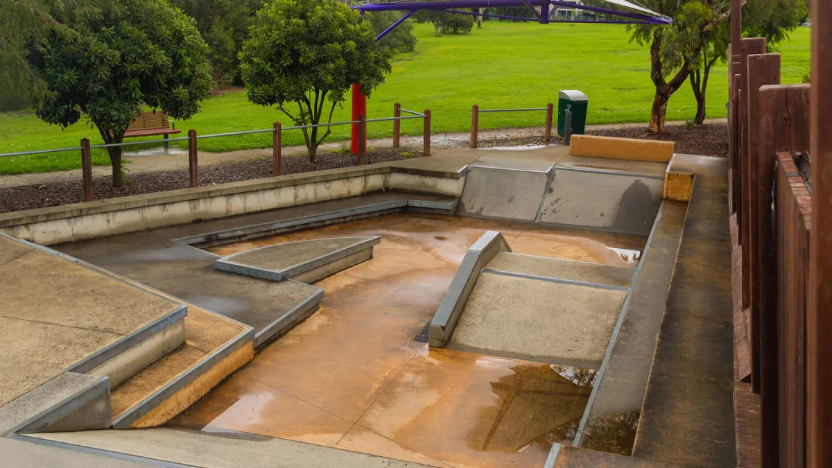 A in-ground skate park with steps and ramps. In the background is a green lawn
