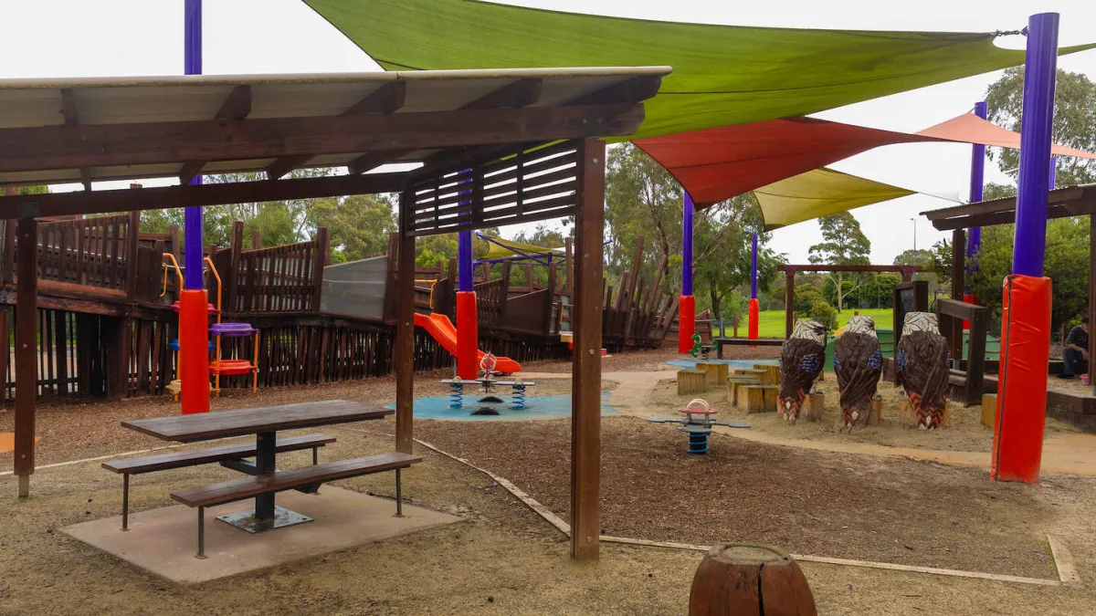 Playground with slides, and 3 bird sculptures and a picnic table under a shelter