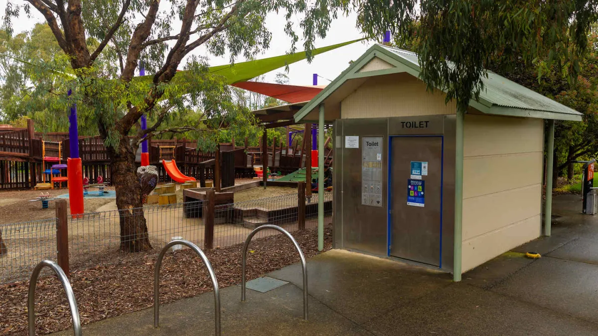 Public toilet, bicycle racks in front of a fenced playground