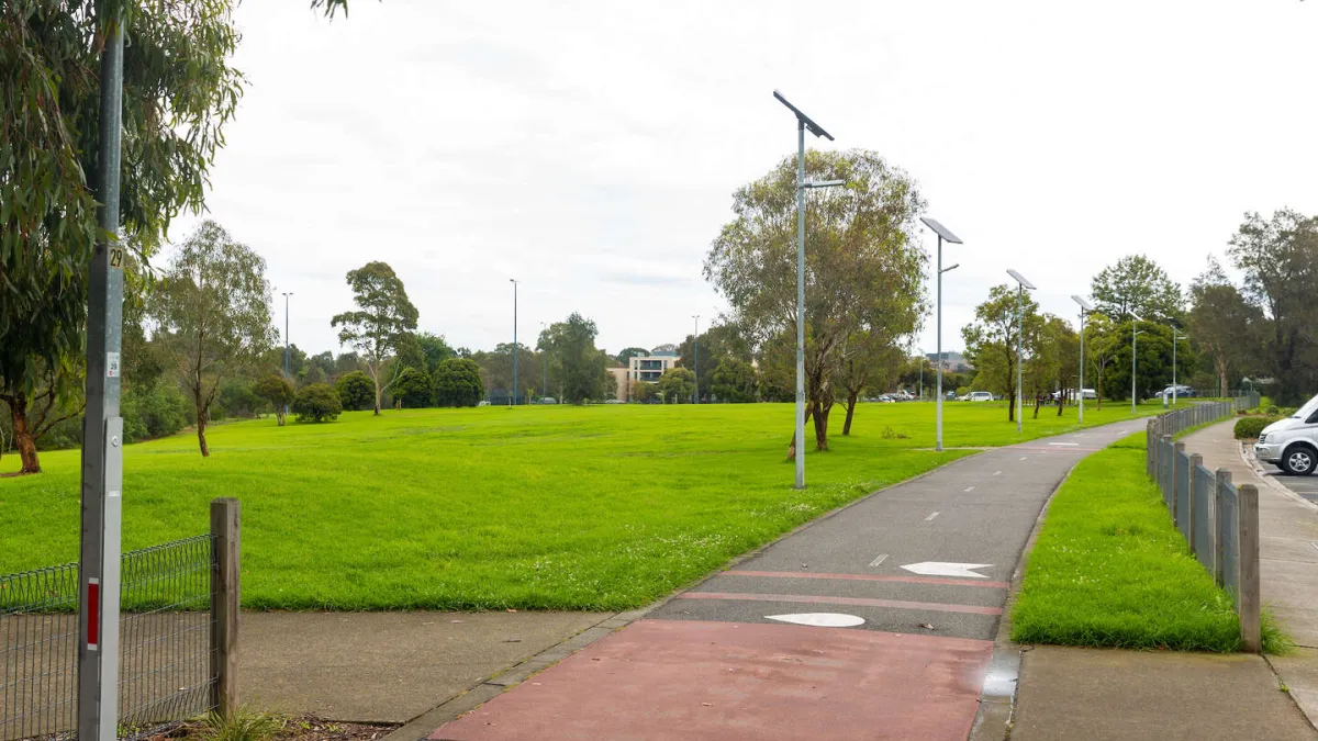 A concrete walking path. Car park is to the right, a grass lawn is to the left. 
