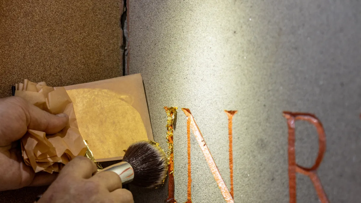 Gold lettering being applied to the stone of the memorial.