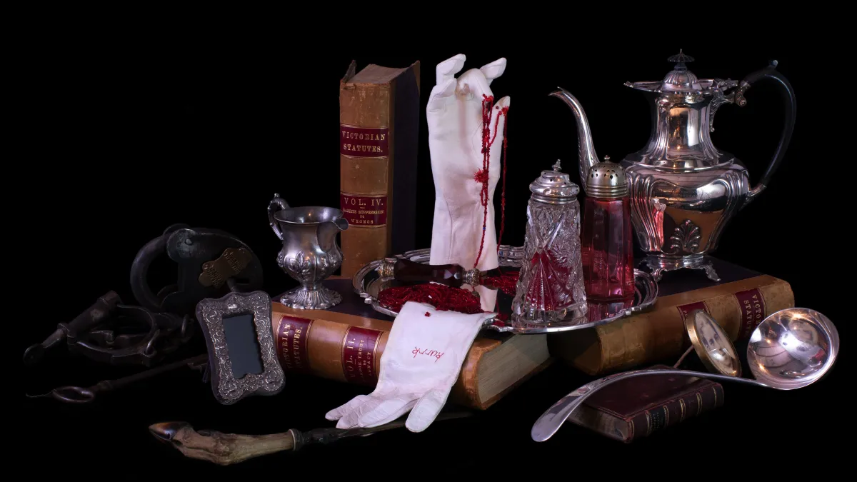 Collection of items including white gloves, silverware, photoframe, books and red thread against a dark background