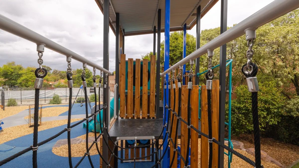 A climbing rope ladder with sun-protection cover at a playground