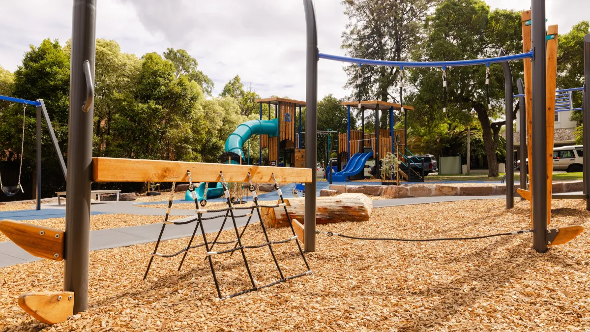 Play area including a small rope ladder and a single horizontal pole at a playground