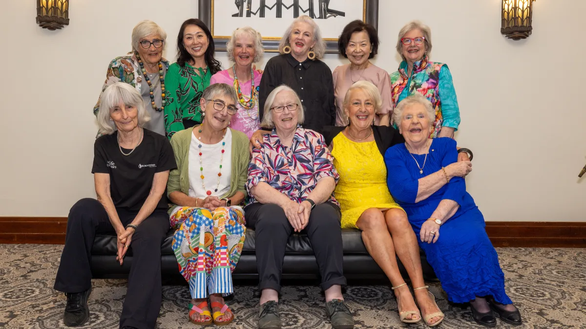 11 women sitting together smiling. They look happy and you can see the connection they have with each other.