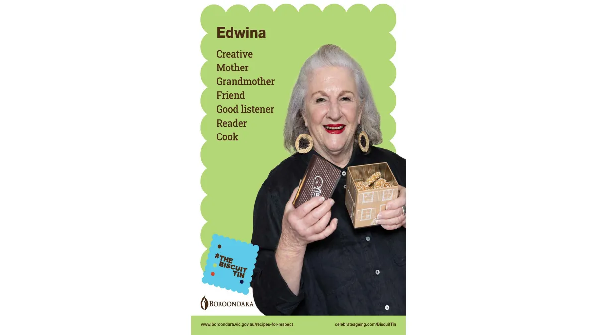 Edwina has shoulder length grey hair with big round earrings. She's holding a house shaped biscuit tin. She is creative, a a good listener, reader, cook, mother, grandmother and friend,