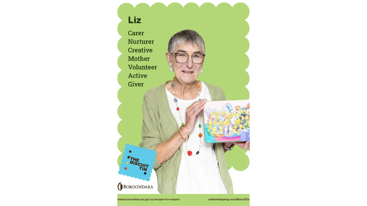 Liz is wearing a pale green shirt, long beaded necklace and large narrow framed glasses. Her biscuit tin has a picture of characters from the Simpsons sitting around the couch watching tv.