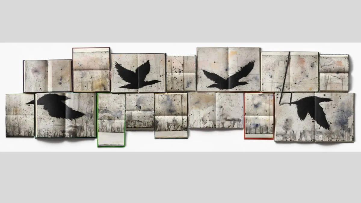 A wide, horizontal artwork composed of multiple open hardcover books. Each book is marked with stains, smudges, and fine lines. Four black silhouettes of flying birds appear across multiple pages.
