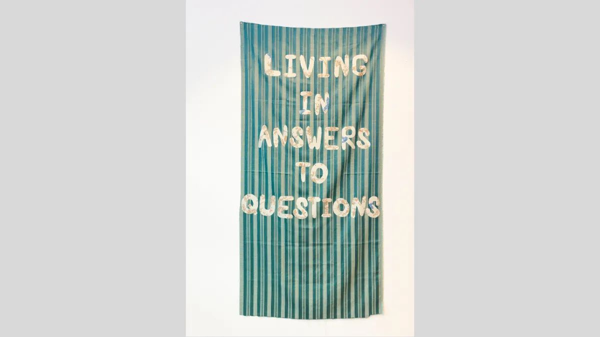 Green striped fabric banner with text that says 'Living in answers to questions'