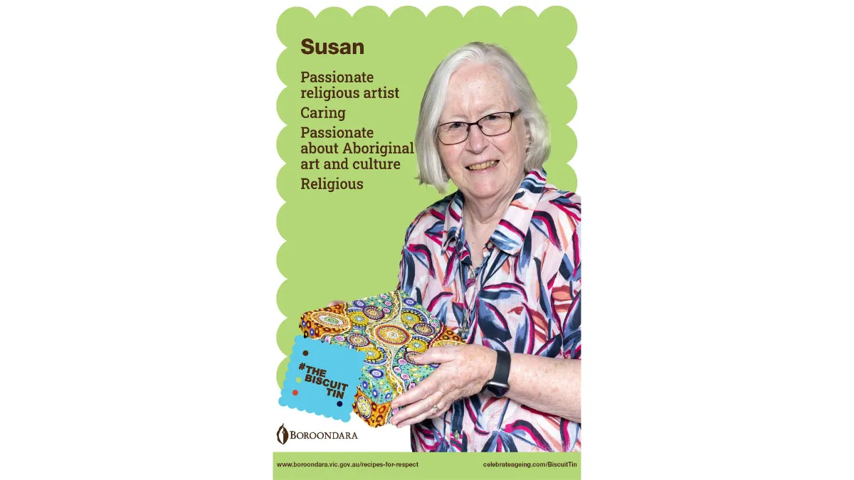 Susan's white hair is cut in a bob, and she's wearing dark framed glasses and pink, blue and white patterned shirt. Her square biscuit tin is covered in a circluar Aboriginal pattern with lot s of colours.
