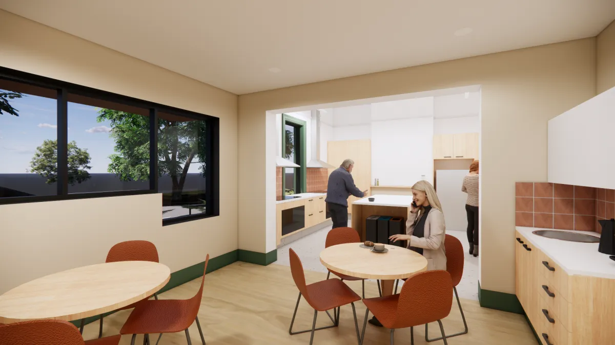 A shared kitchen and social space. It has windows looking to outside, and small tables where people can work or casually meet.