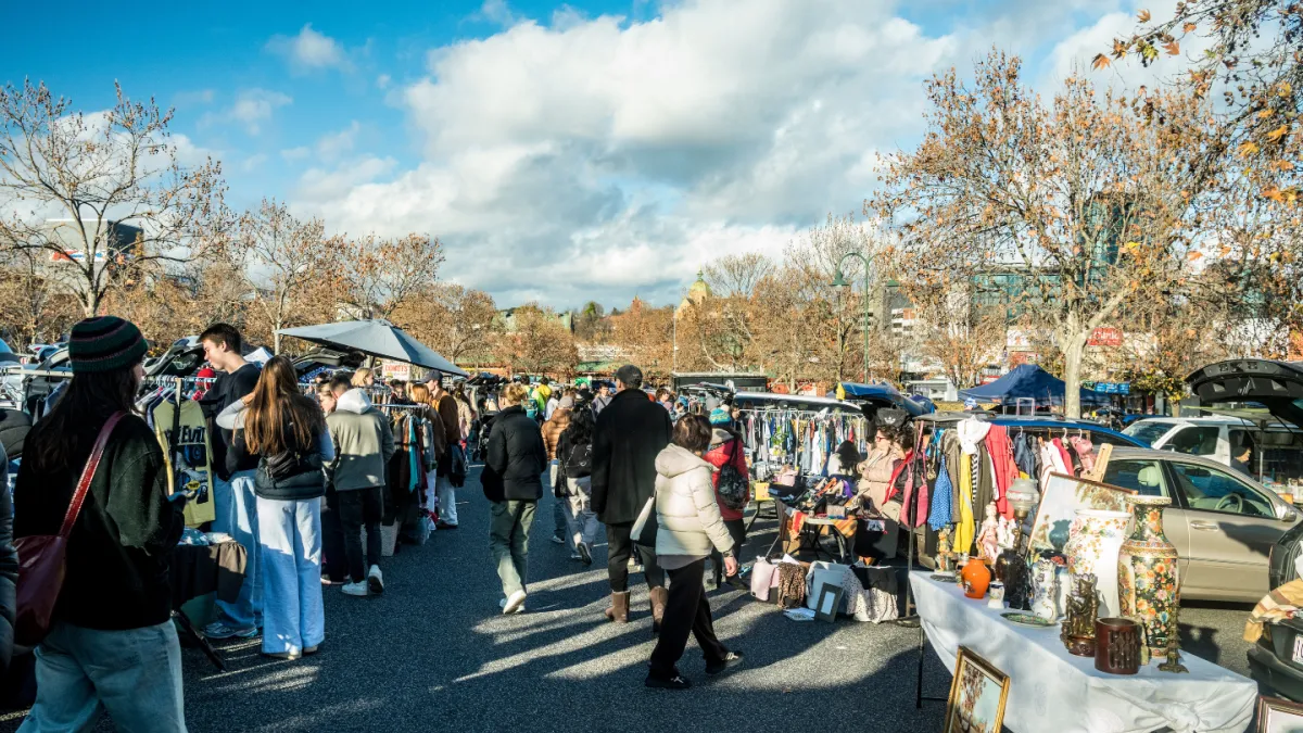 A sunny market day with busy stall and people walking around.