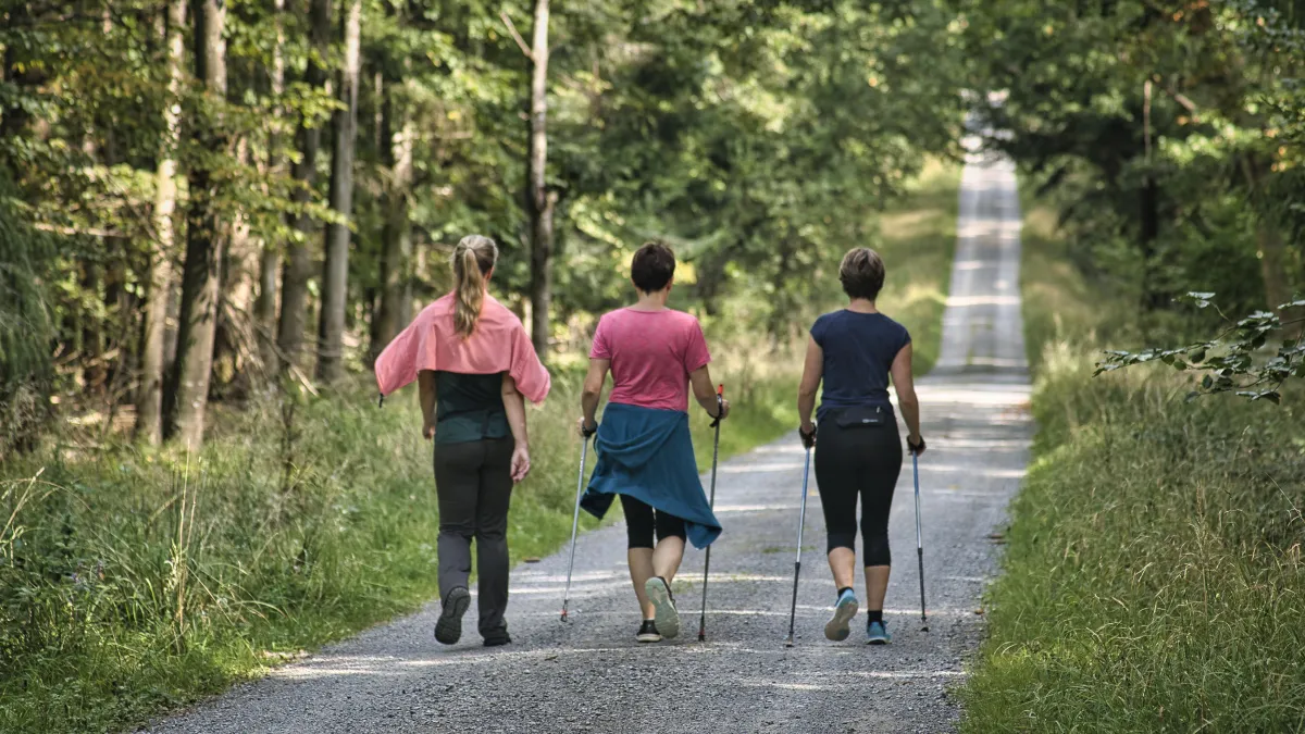 Three women walking along a gravel track. two are using walking poles. all are wearing athletic clothing.