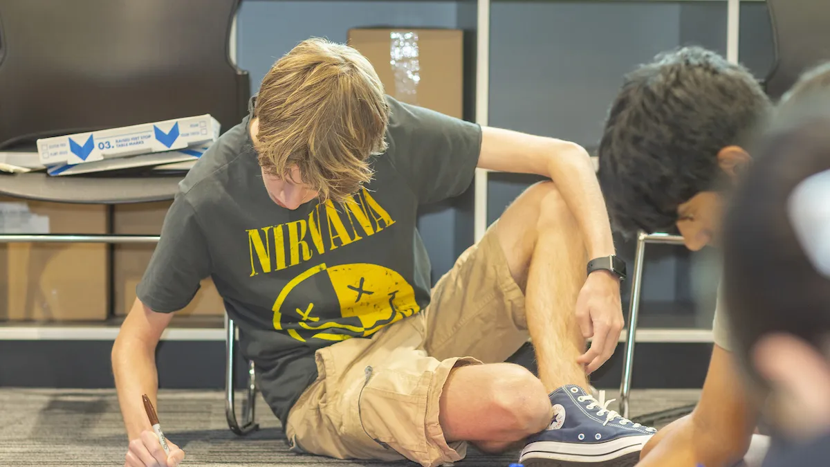 Young people sitting on the floor  writing on paper.