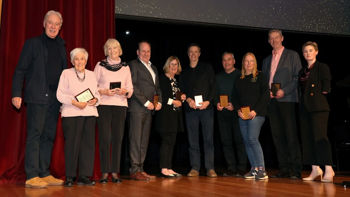 10 people are smiling at the camera. 8 of them are holding plaques. 