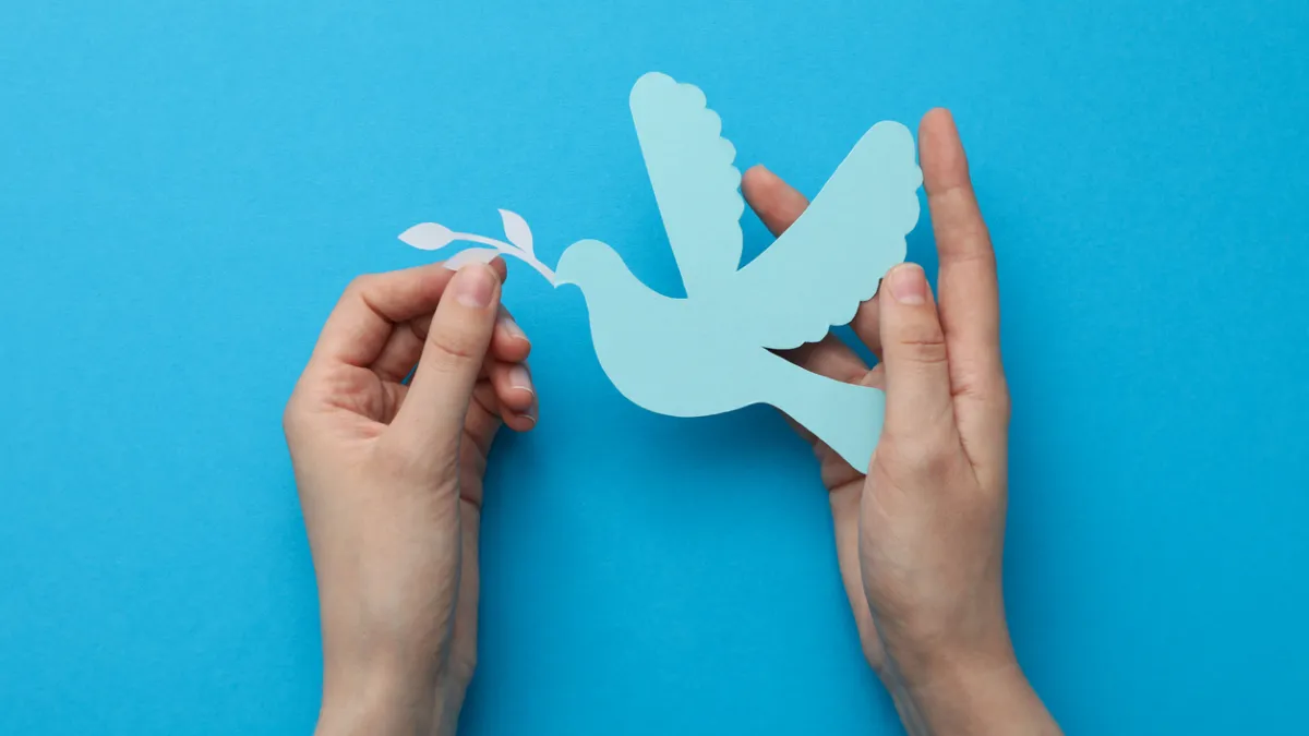 Two hands holding a light blue paper silhouette of a dove.