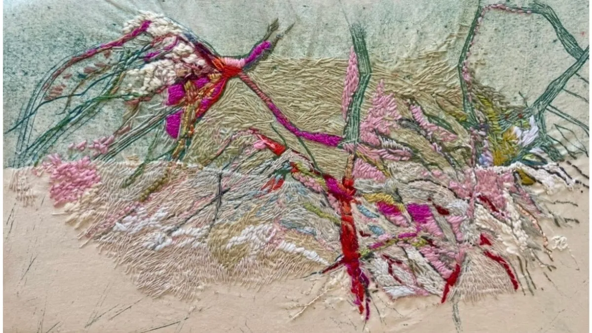 Textile artwork of stitched abstract forms made with dense embroidery. Pink, red, white and green threads create layered lines, textured shapes and woven patterns across a pale fabric background.