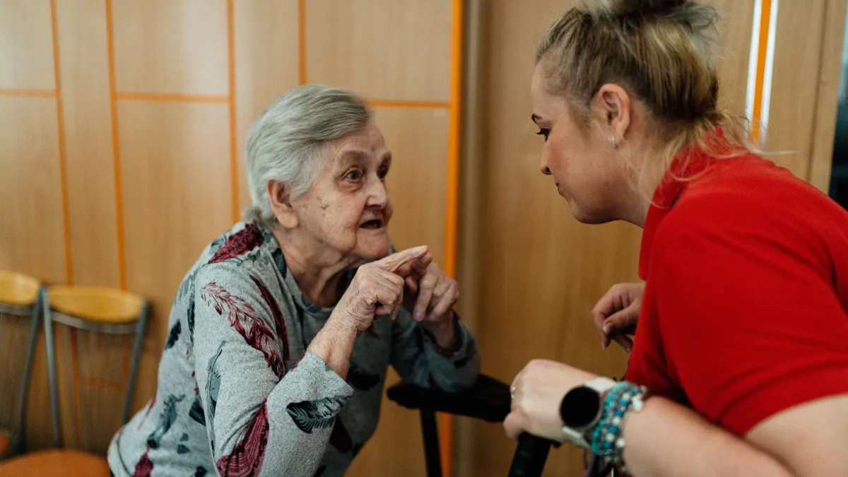 A senior citizen is getting help from a carer to stand.