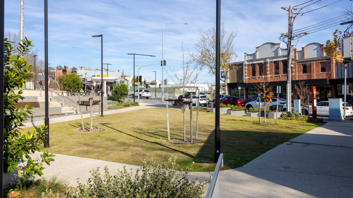 A green area with tiered seating is adjacent to a row of shops.