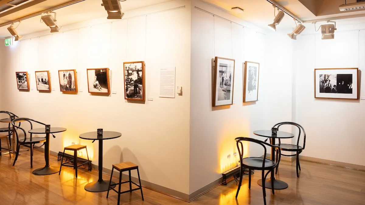 Black and white photographs installed on a white wall. Tables and chairs in front of photographs. 