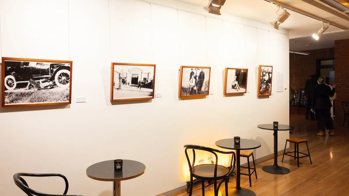 Black and white photographs installed on a white wall. Tables and chairs in front of photographs. 