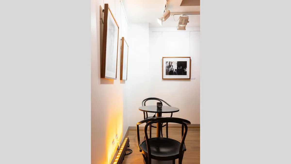 Black and white photographs installed on a white wall. Tables and chairs in front of photographs. 