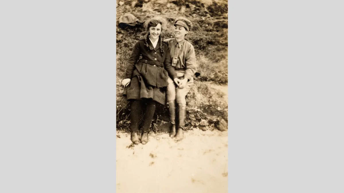 Old sepia photograph of two figures seated and holding hands