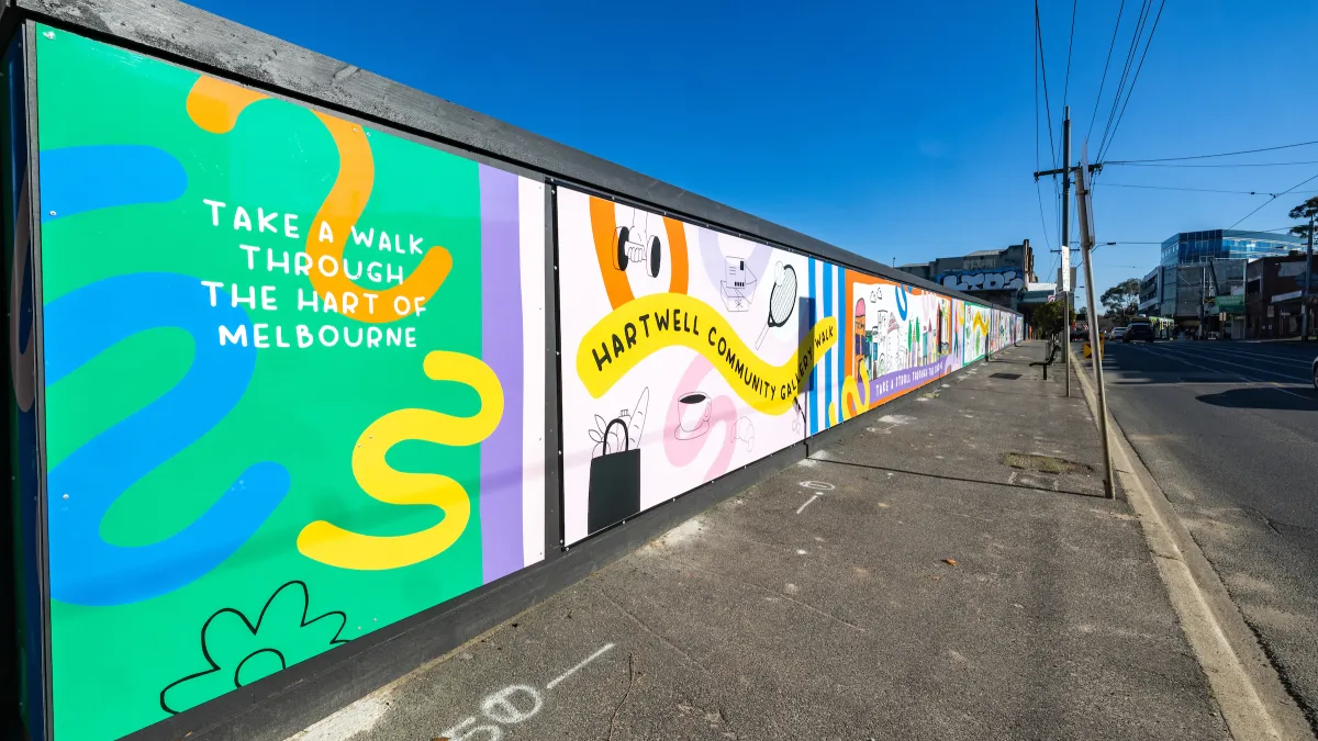 Worksite cladding adorned with a mural inviting passersby to "take a walk through the HART of Melbourne. with squiggly lines and illustrations leading down the road.