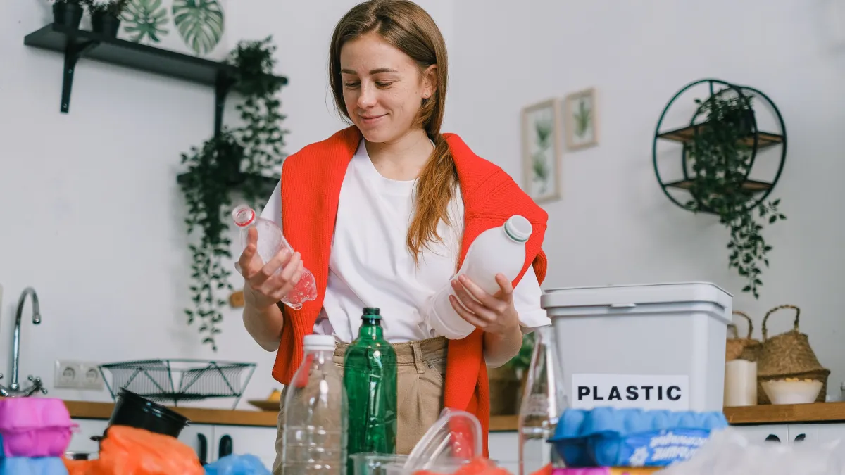 A young woman sorts plastic bottles for recycling in a kitchen environment