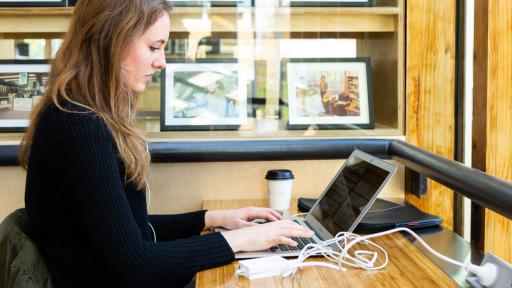 Woman sitting at a desk with a coffee and a laptop, typing.