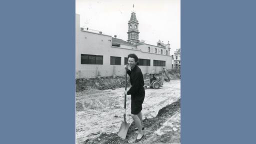 Black and white photograph of Jane Nathan digging on a building site with Hawthorn Town Hall in the background