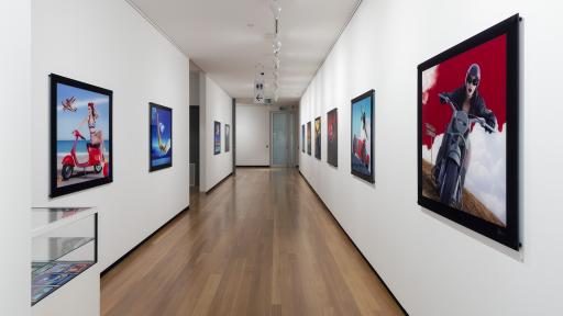 View of a corridor gallery space, with large square artworks hanging on either side.