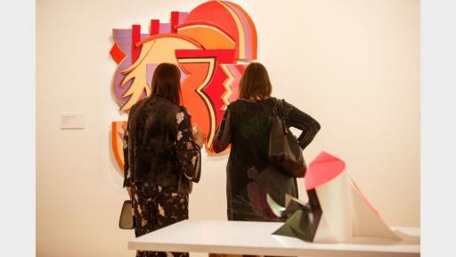 Visitors to 'Light Gestures' looking at a mixed media artwork made up of abstract geometric shapes.