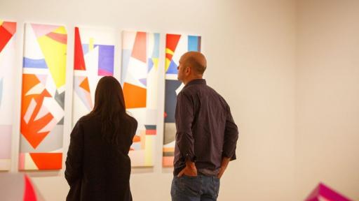 Visitors to 'Light Gestures' looking at an artwork made up of long skinny panels, covered in abstract geometric shapes.