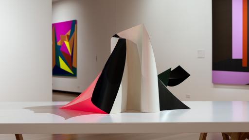 Installation view of 'Light Gestures' at Town Hall Gallery. Abstract geometric paintings on the wall. Abstract sculpture on a table, made up of large flat surfaces and lots of angles.