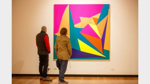 Visitors to 'Light Gestures' looking at a painting covered in abstract geometric shapes.