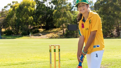 Young cricketer holding a cricket bat and standing in front of stumps.