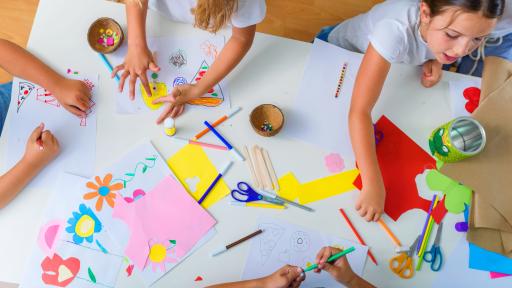 Children painting and drawing together across pieces of paper