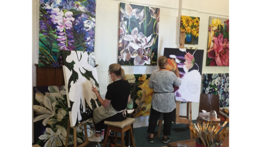 Two women at easels working on large scale detail paintings of flowers.