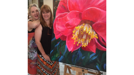 Artist Shani Alexander with a participant from one of her workshops. Participant is holding a large painting of a camelia flower up close.