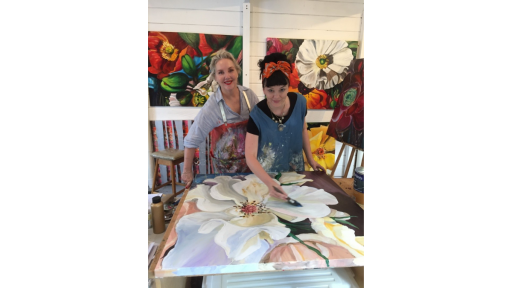 Artist Shani Alexander with a participant from one of her workshops. Participant is leaning over a large painting of a flower up close.