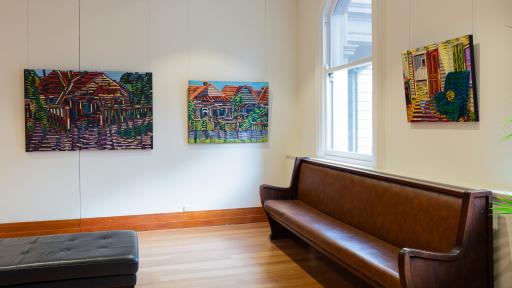Two paintings on the left are of the exterior of houses, created out of lots of lines of colour. On the right, the interior of a room, a comfy armchair is the feature.