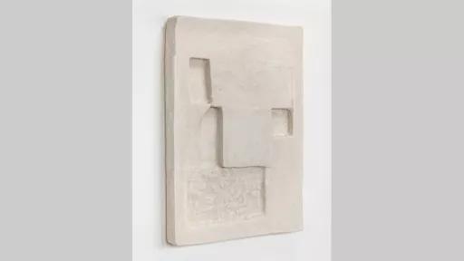 A flat rectangular form on a wall, with geometric shapes indented into it.