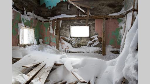 Inside a derelict building, filled with piles of timber covered in snow.